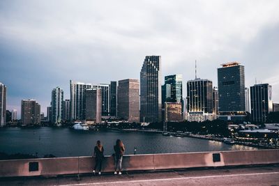 Rear view of women standing on bridge against cityscape