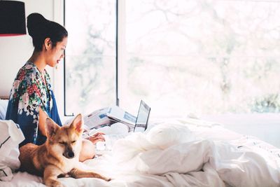 Dog sitting by woman using laptop on bed at home