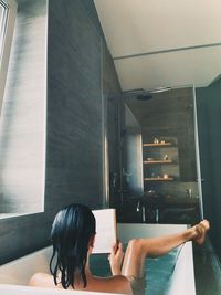 Rear view of woman reading book in bathtub at home