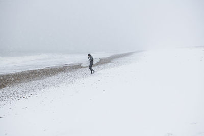 Man walking on snow covered land against sky