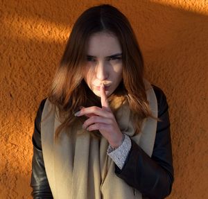 Close-up portrait of young woman gesturing against wall