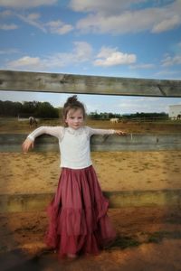 Portrait of cute girl standing on land by fence against sky