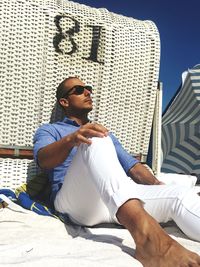 Handsome young man sitting by hooded beach chair during sunny day