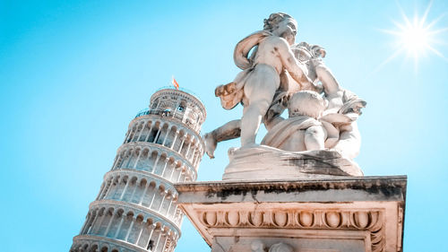 Leaning tower of pisa and statue of cherubs winged angels supporting heel of tower and shining fair 