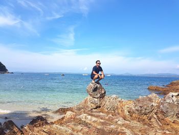 Man standing on rock in sea against sky