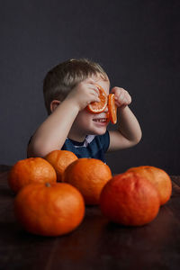 Cute boy holding orange slices on eyes at home