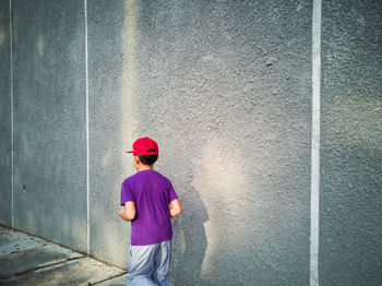 Boy running on footpath by concrete wall