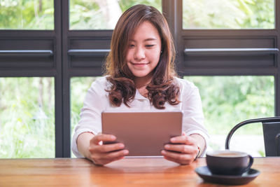 Woman using digital tablet by coffee cup while sitting on table