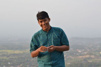 Smiling young man standing against sky