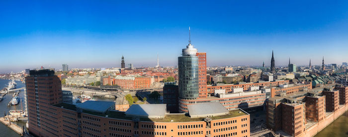 Aerial view of buildings in city against blue sky