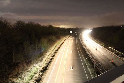 Road amidst illuminated trees against sky at night