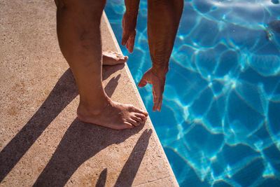 High angle of crop anonymous barefoot person stretching forward while standing on poolside edge near clean water person