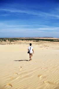 Rear view of man walking on sand in desert against sky