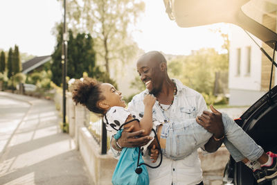 Cheerful man carrying daughter by electric car on driveway