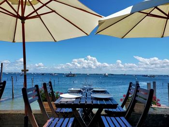 Empty chairs and table by sea against sky