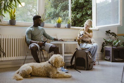 Young man looking at woman stroking dog in waiting room at medical clinic
