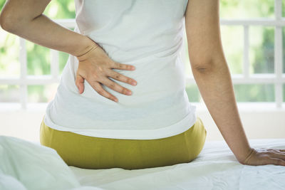 Midsection of woman suffering from backache sitting on bed at home