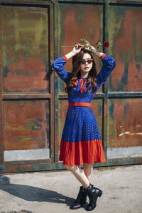 Full length of young woman holding rose against metallic gate