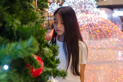 Girl standing by illuminated christmas tree