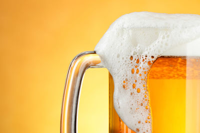 Close-up of beer glass against orange background