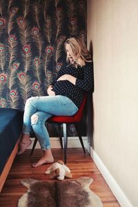 Pregnant woman sitting on chair against wall in bedroom