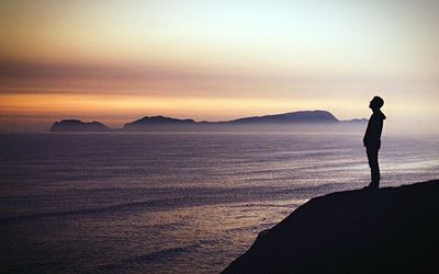 Silhouette man standing on shore against sky during sunset