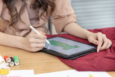 Midsection of woman using digital tablet on table