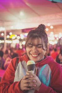 Smiling woman holding ice cream cone in illuminated city at night