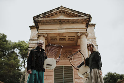 Couple holding lyra musical instrument against built structure