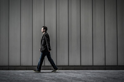 Side view of man walking on sidewalk by wall