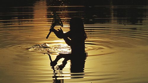 Silhouette woman standing by lake during sunset