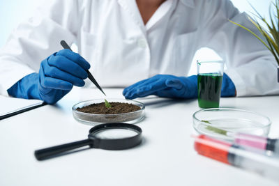 Midsection of doctor examining plant and mud on table