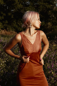 Side view of young woman standing against plants