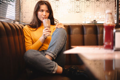 Thoughtful teenage girl drinking chocolate milkshake in restaurant