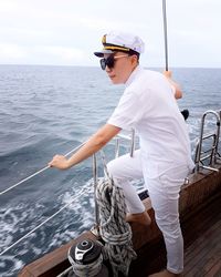 Side view of sailor wearing uniform looking at sea while standing on ship