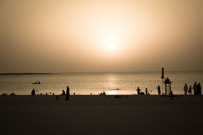 Silhouette people on beach against sky during sunset