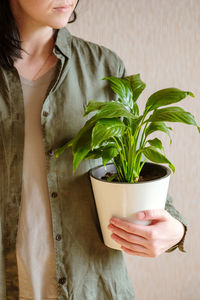 A woman with dark hair in a green shirt in her hands a beautiful spathiphyllum flower in a white pot