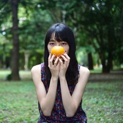 Portrait of young man eating orange  against trees