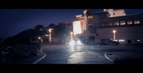 Vehicles on road in front of illuminated buildings at night