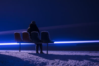 Person sitting on bench against light trails at night during winter