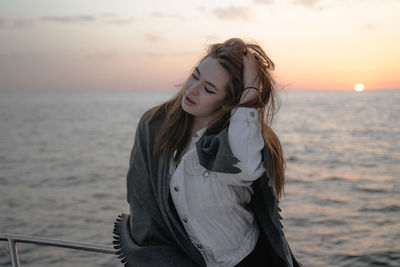 Portrait of young woman standing against sea during sunset