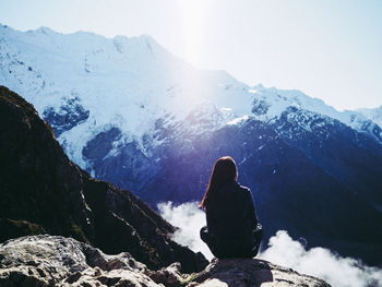 Woman sitting on rock while looking at snowcapped mountains