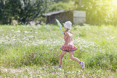 Side view of girl holding butterfly net while running amidst plants on field