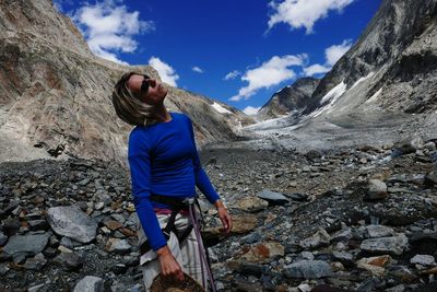 Senior woman standing on rocks with mountains in background
against sky