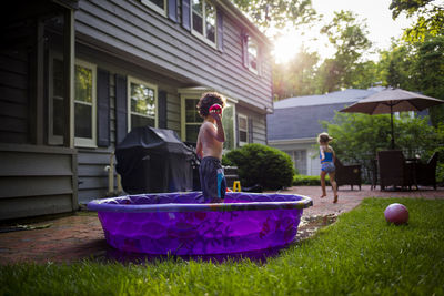 Girl running while brother standing in wading pool at backyard
