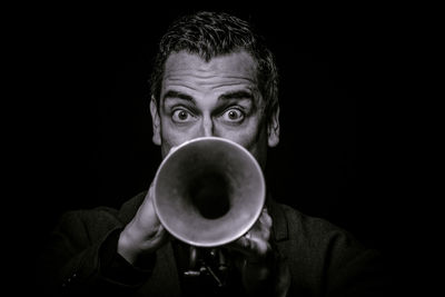 Close-up portrait of man playing trumpet against black background