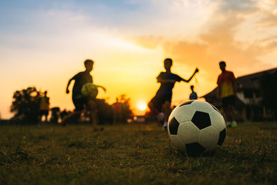 People playing soccer on field against sky during sunset