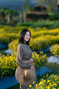 Portrait of smiling young woman standing against yellow flowering plants