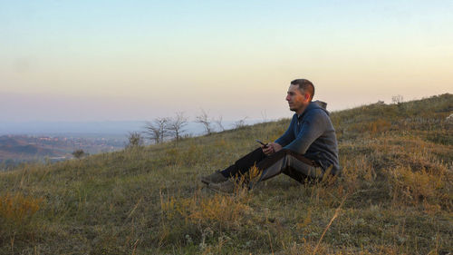 Side view of man sitting on field against sky during sunset