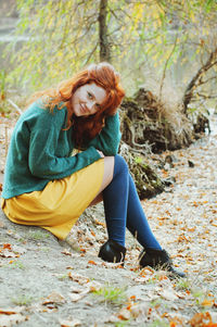 Full length of young redhead woman with freckles sitting on land